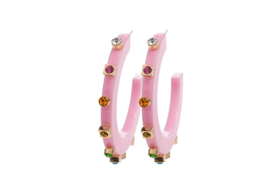 Two pink acrylic hoop earrings standing upright against a white background, adorned with colorful gemstones in gold settings with vibrant reflections.