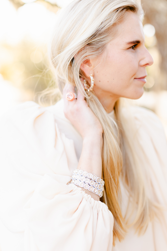 Smith wears metallic silver hoop earrings and a jeweled bracelet, with soft lighting highlighting the sparkle of the jewelry against a sunlit background.