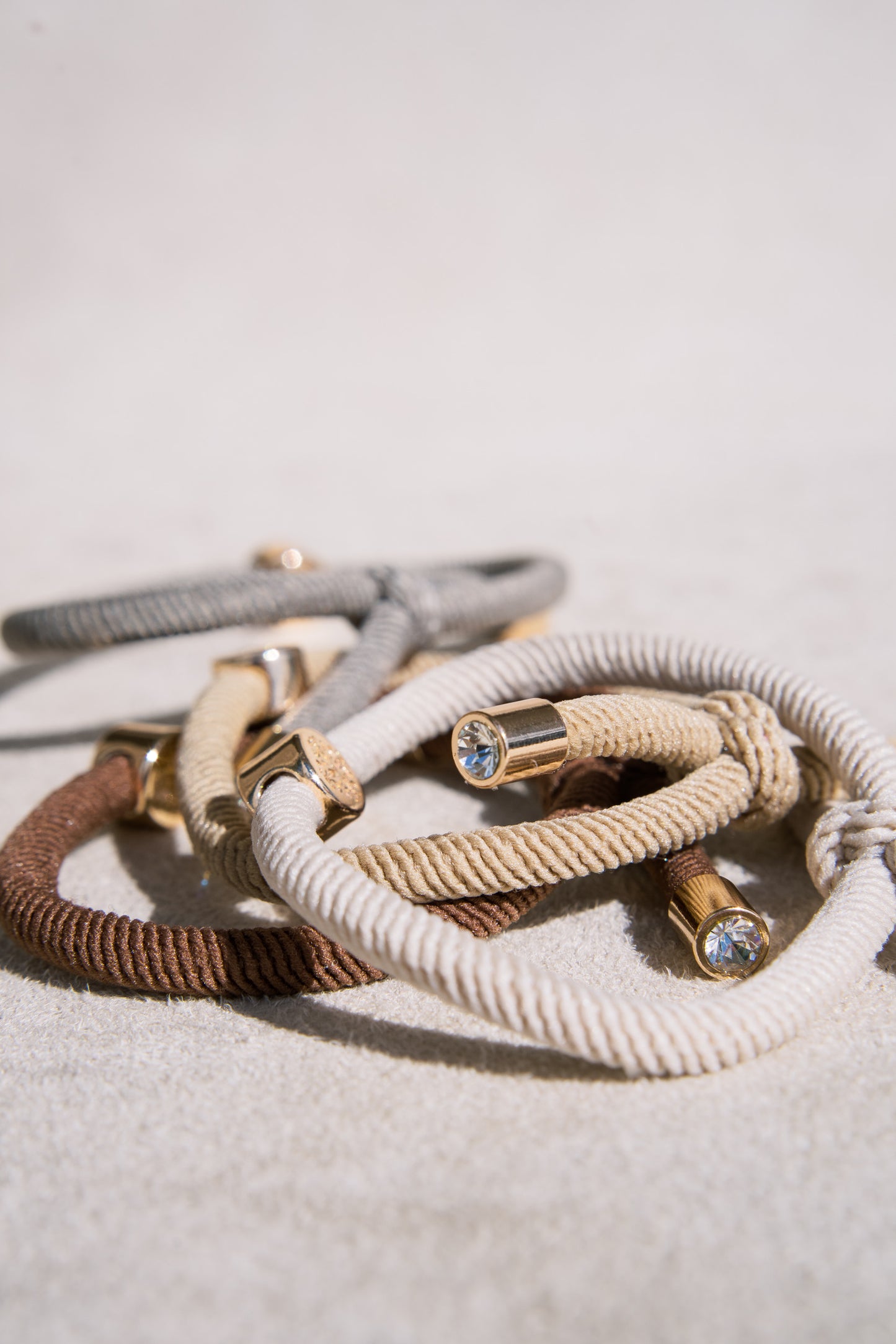 Neutral tone elastic hair ties featuring gold accents and crystal details, offering a sophisticated and durable accessory for hair or wristwear.