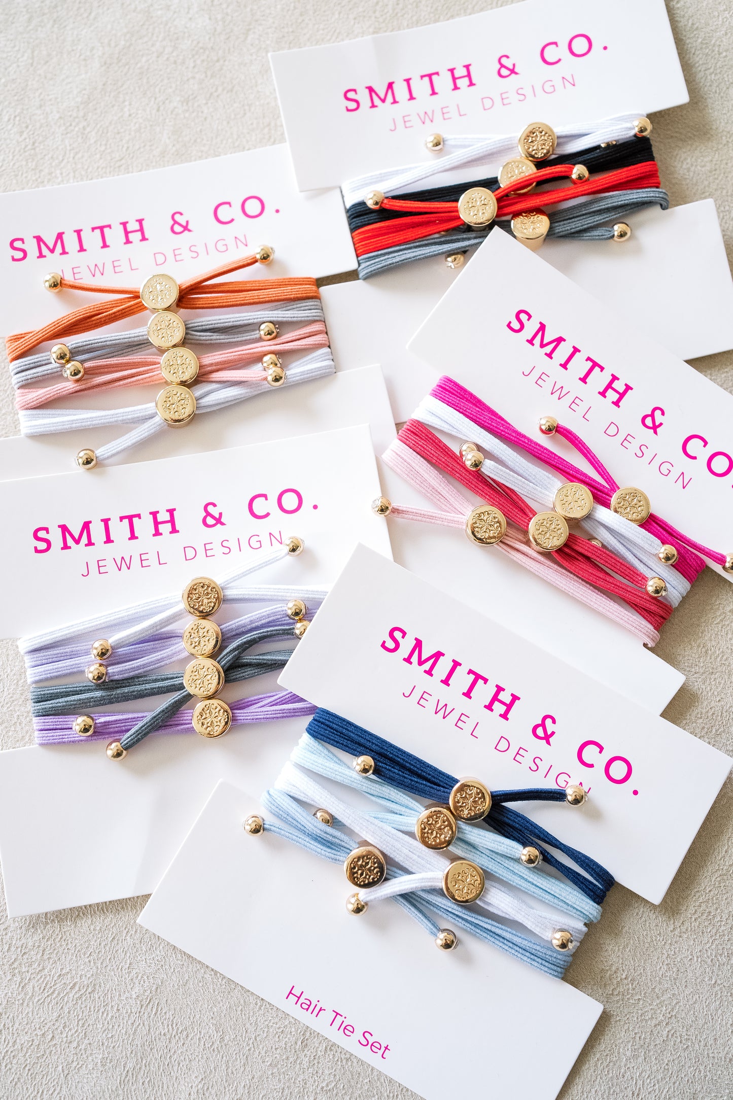 Smith & Co. skinny hair tie sets featuring multiple vibrant color combinations with gold accents, elegantly packaged, perfect for hair or wrist wear.