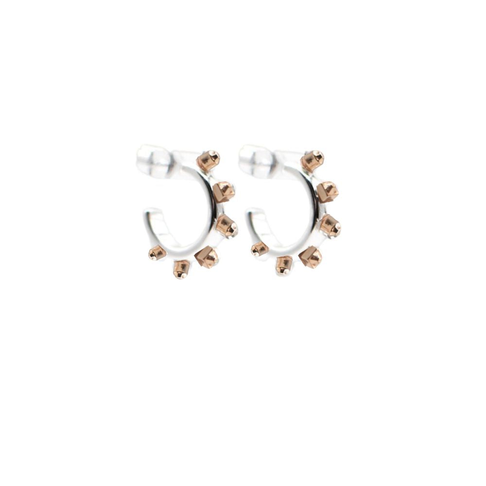 Close-up shot of a pair of matte silver huggie hoop earrings with matte gold spike accents, placed against a white background for clear detail and focus.