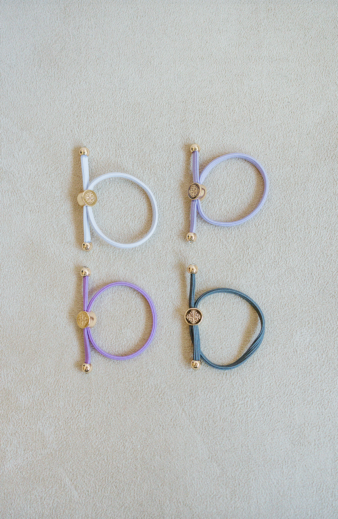 Sold as a set of 4, Children's Size single strand skinny Hair Tie Set are bracelets with round gold end caps and signature gold detail in purple, grey, and white.