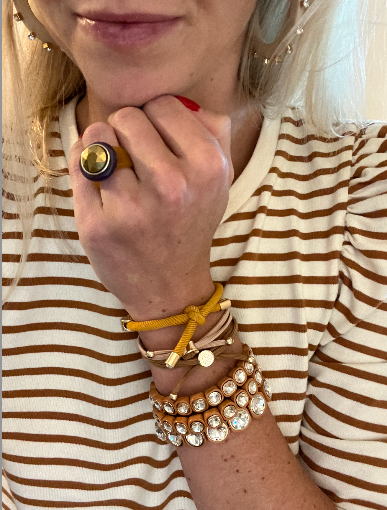 Showcases layered wrist accessories: vibrant knotted cord bracelets in mustard yellow and neutral tones, paired with sparkling crystal-studded bangles.