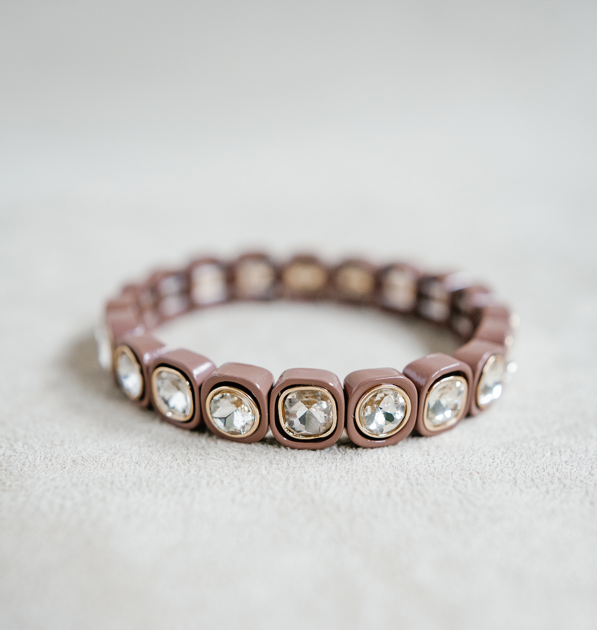 A brown stretch bracelet with glossy square links, each featuring a clear, faceted crystal inset in gold trim, arranged evenly around the band.