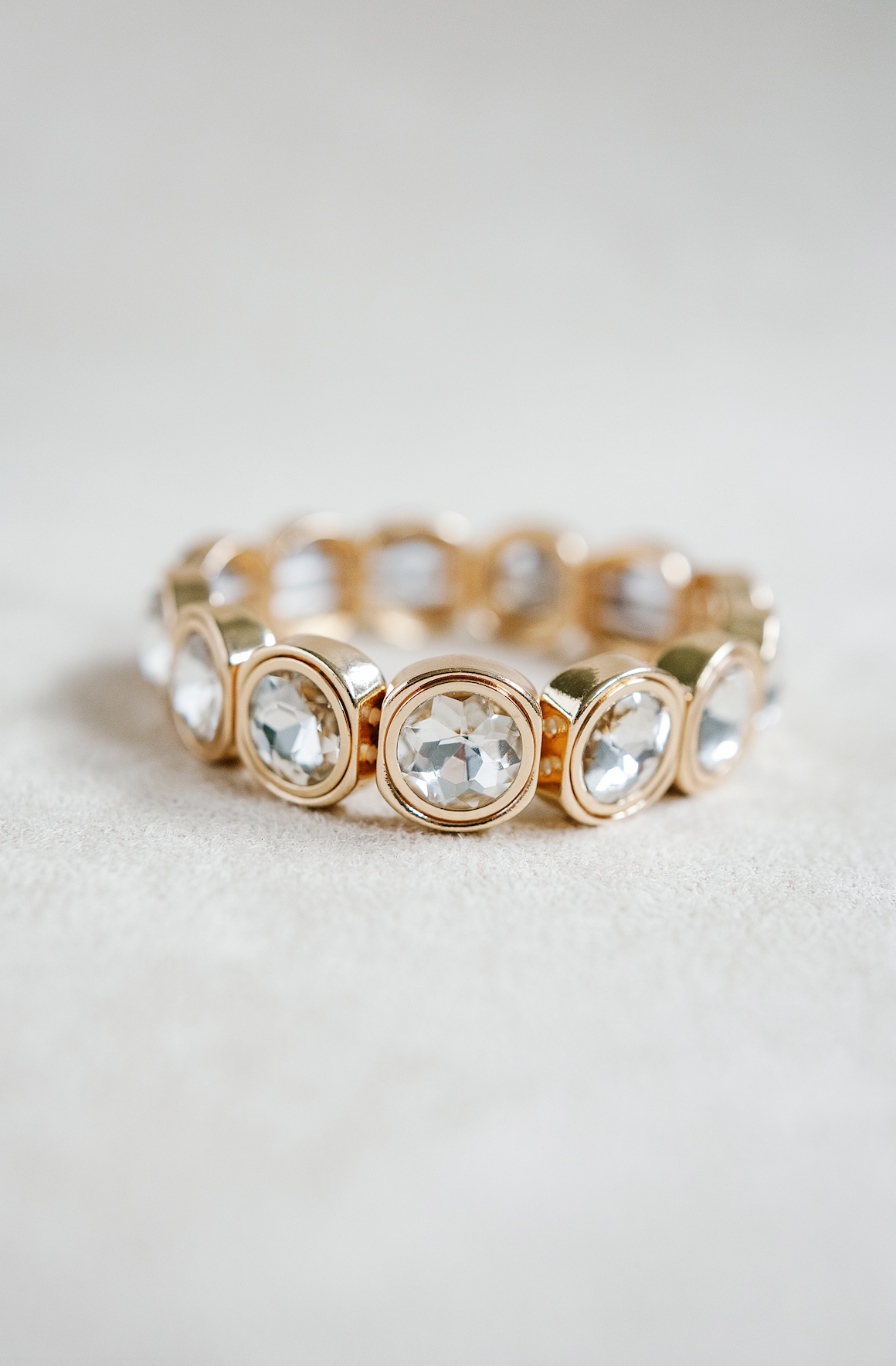 A gold-toned bracelet with circular crystal accents, each housed in rounded square frames, arranged symmetrically around the band for a reflective effect.
