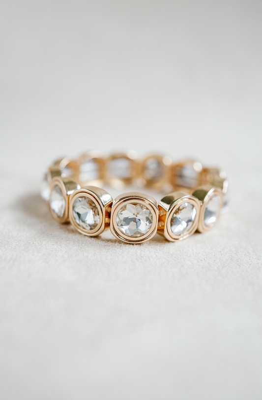 A gold-toned bracelet with circular crystal accents, each housed in rounded square frames, arranged symmetrically around the band for a reflective effect.