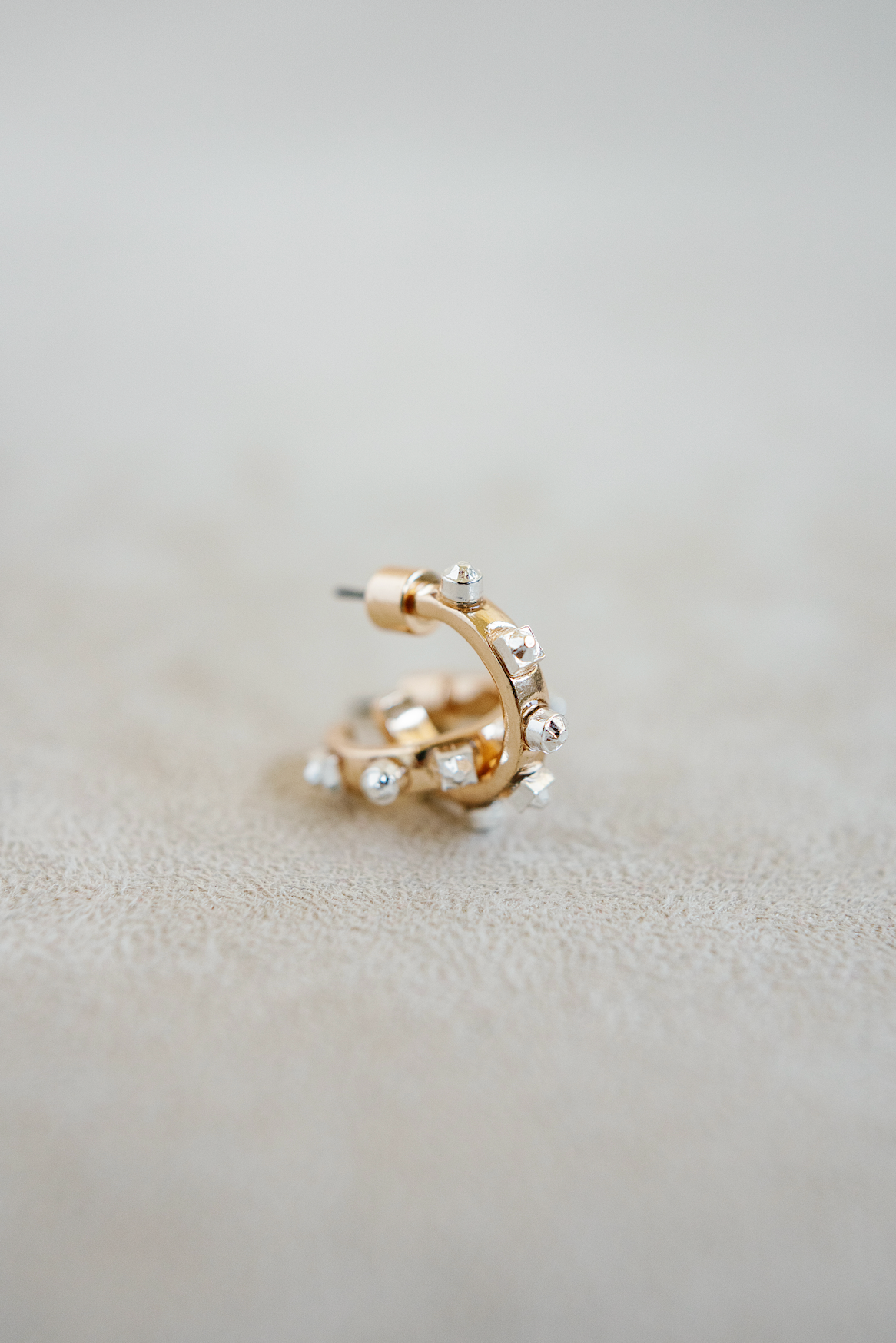 A pair of small, open hoop earrings with a gold-toned finish and silver-tipped studs surrounding the outer edge,