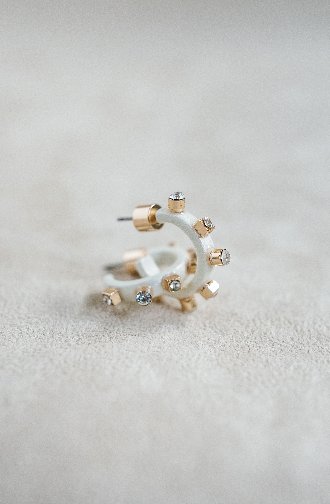 A pair of matte metal white hoop earrings with gold accents, featuring studs around the rim and clear crystals on the post