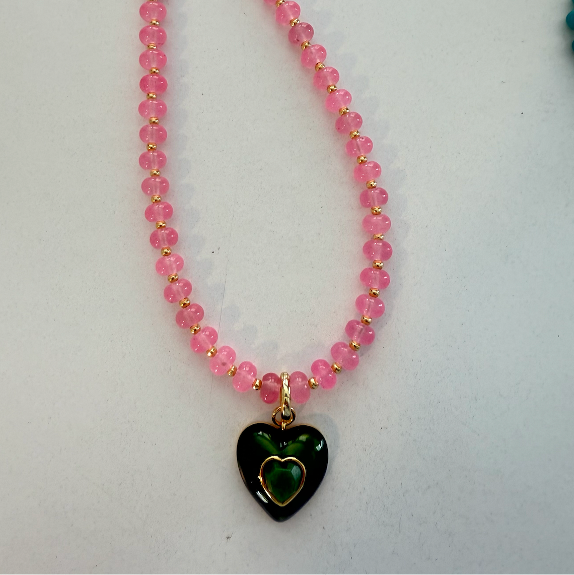 Necklace with pink beads and a green heart pendant on a white background