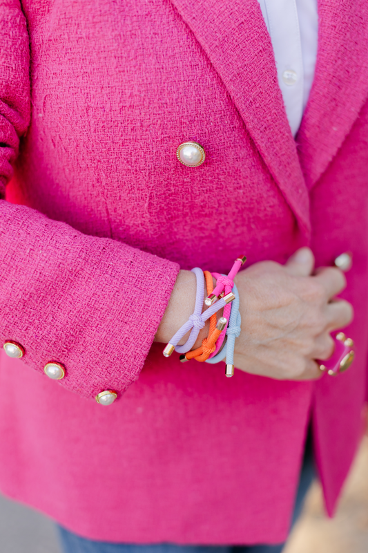 Smith wearing four vibrant knotted hair ties in shades of purple, orange, pink, and blue on her wrist, complimenting her bright pink blazer.