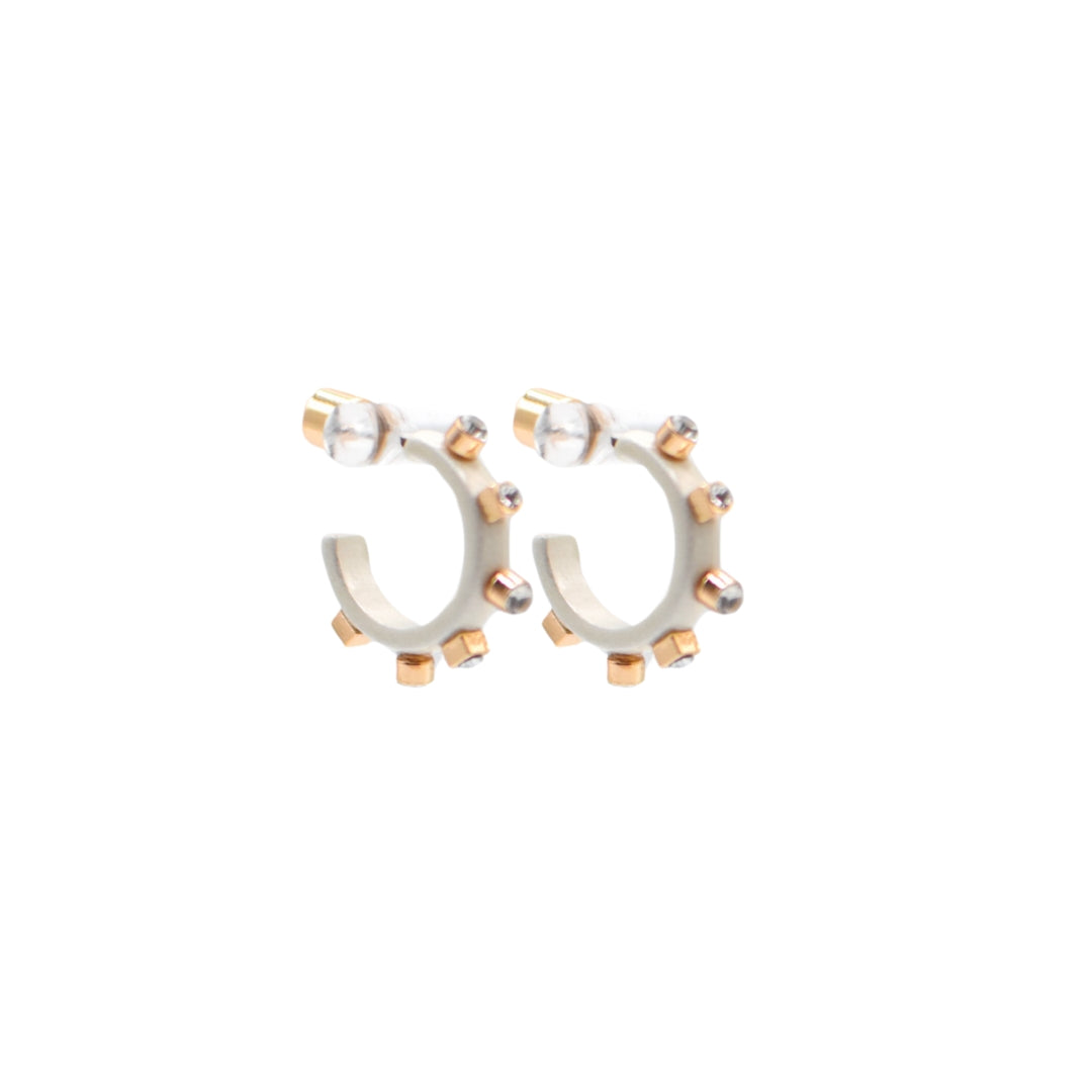 A pair of matte metal white hoop earrings with gold accents, featuring studs around the rim and clear crystals on the post, on a plain white background.