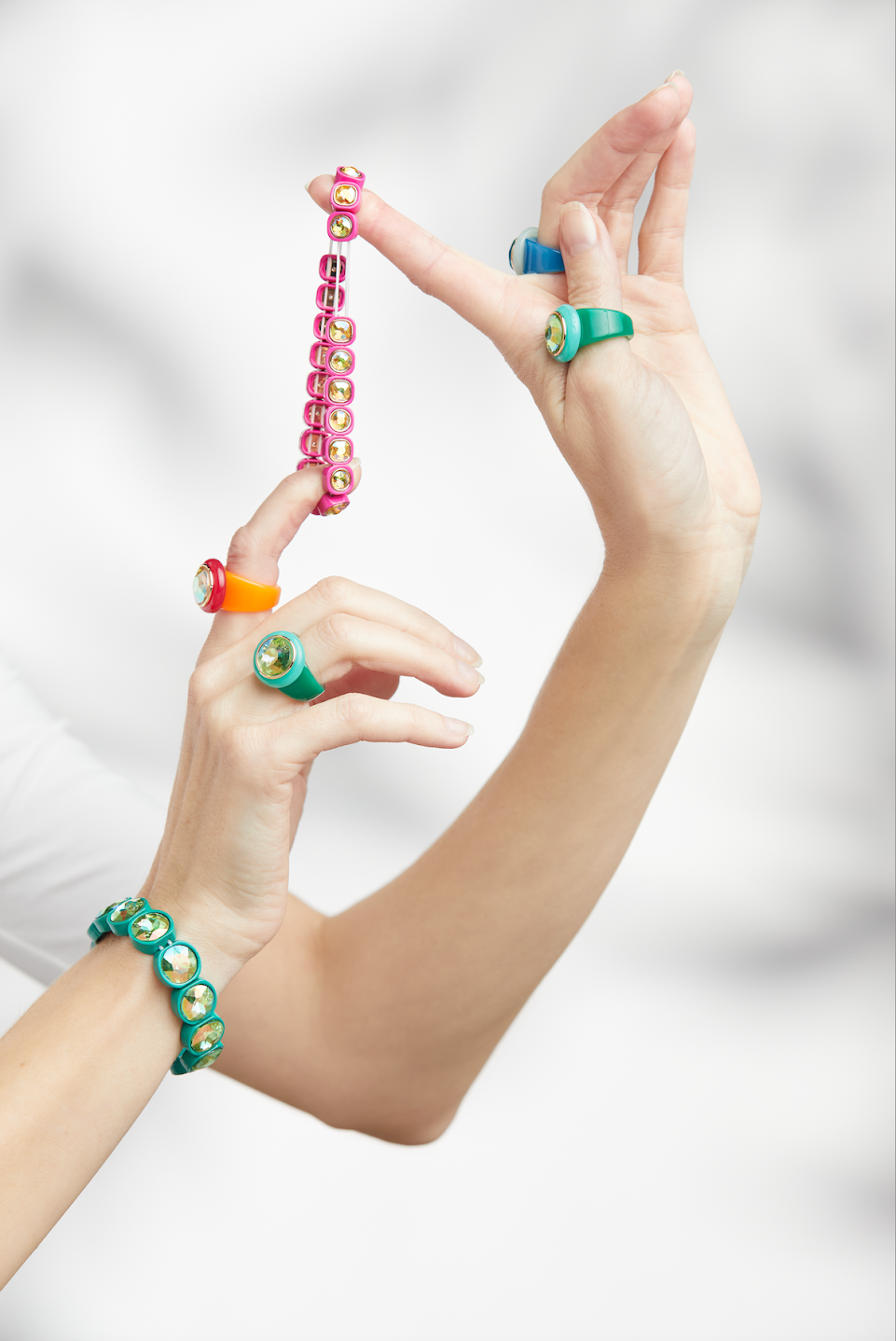 Two hands pose playfully, wearing vibrant acrylic rings and bracelets, highlighting the colorful designs and playful style of the accessories.