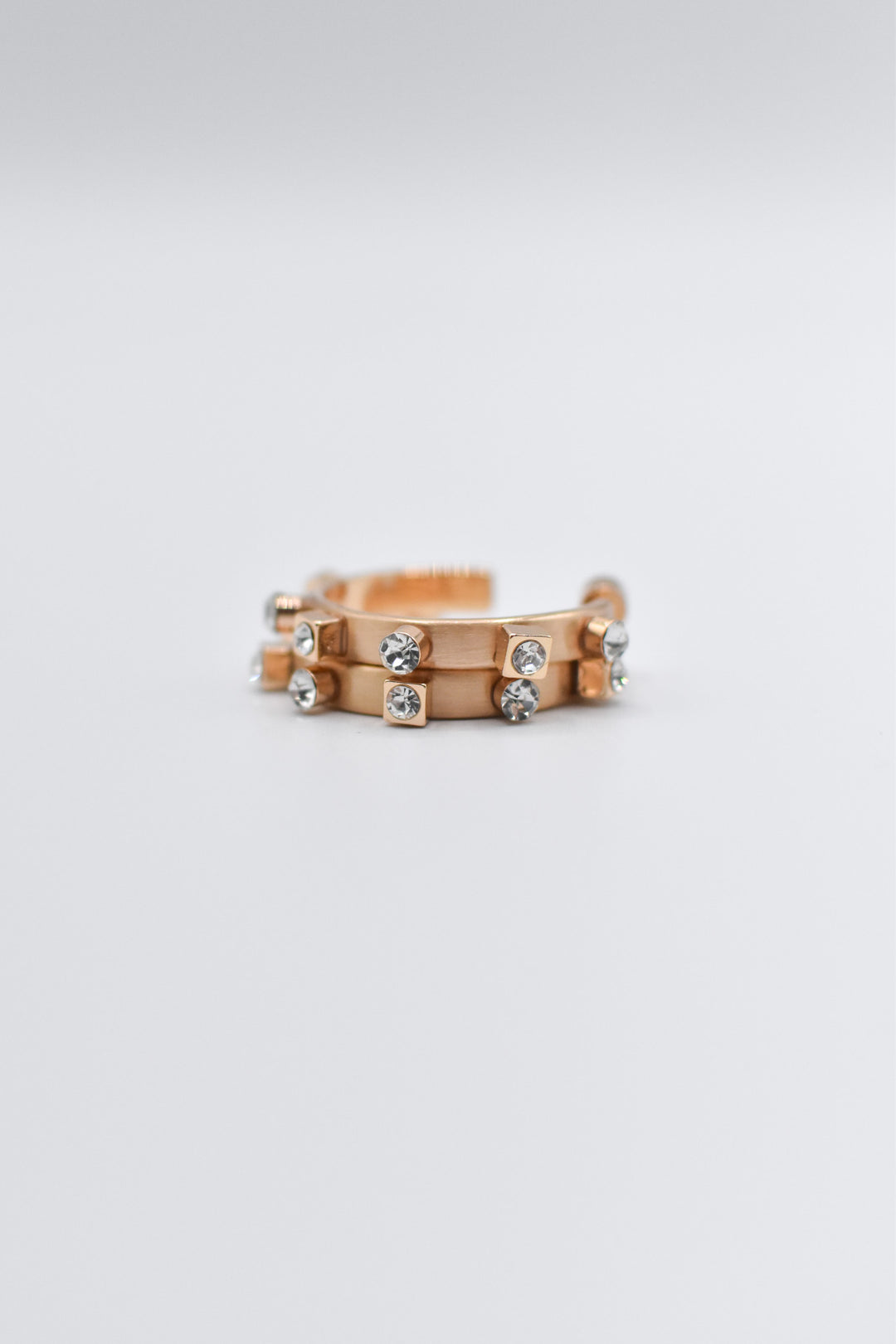 A pair of brushed metallic gold metal hoops decorated with matte silver square and round studs lay stacked neatly on a plain, light-colored background.