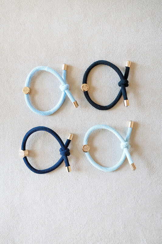 "Four elastic hair ties in shades of light blue, navy, and black, arranged on a soft surface with gold accents, showcasing their textured design.