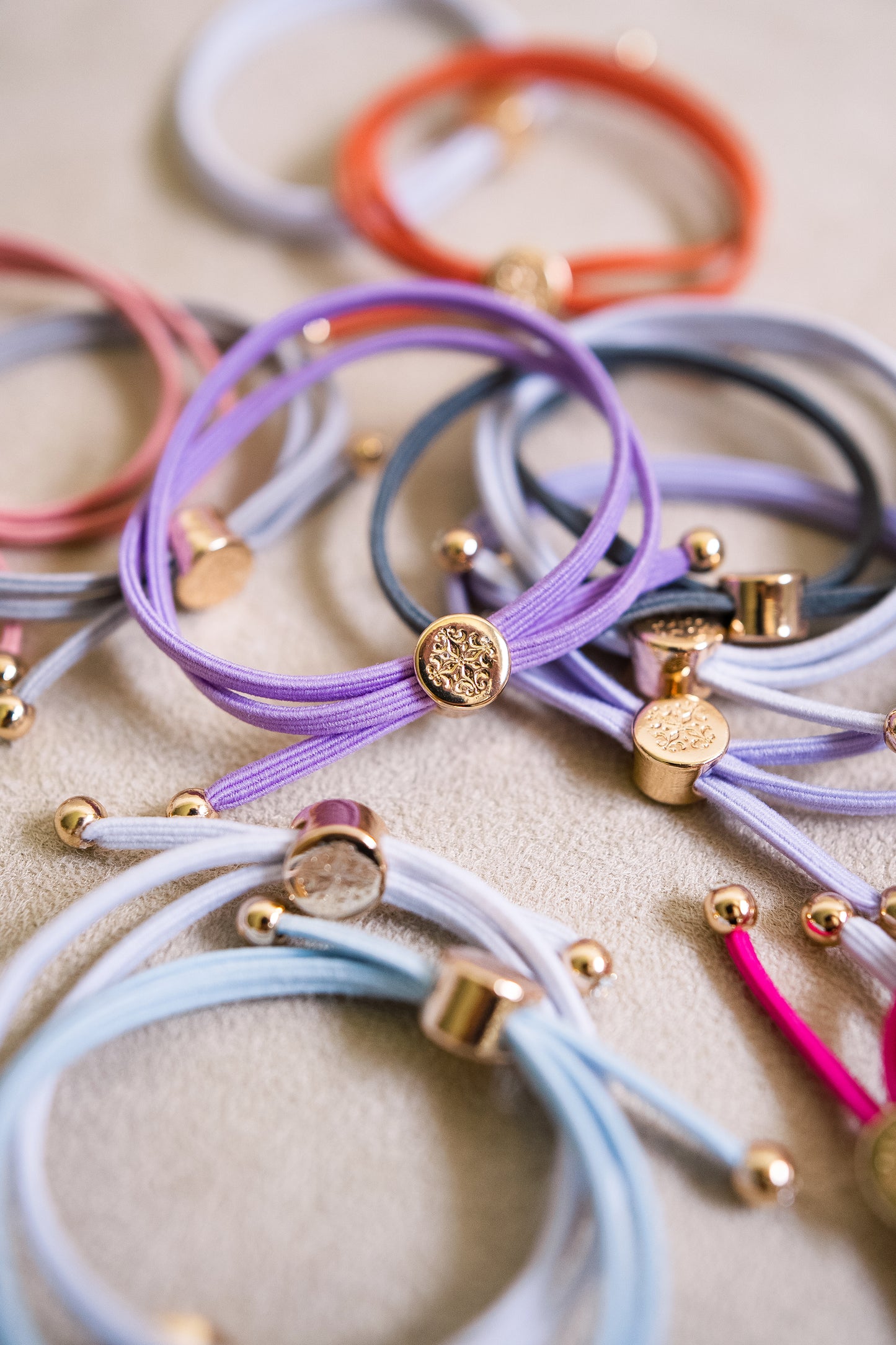 Assorted elastic hair ties in vibrant colors like lavender, blue, and orange, with a close look at Smith & Co.'s logo detailed on center the gold charm.