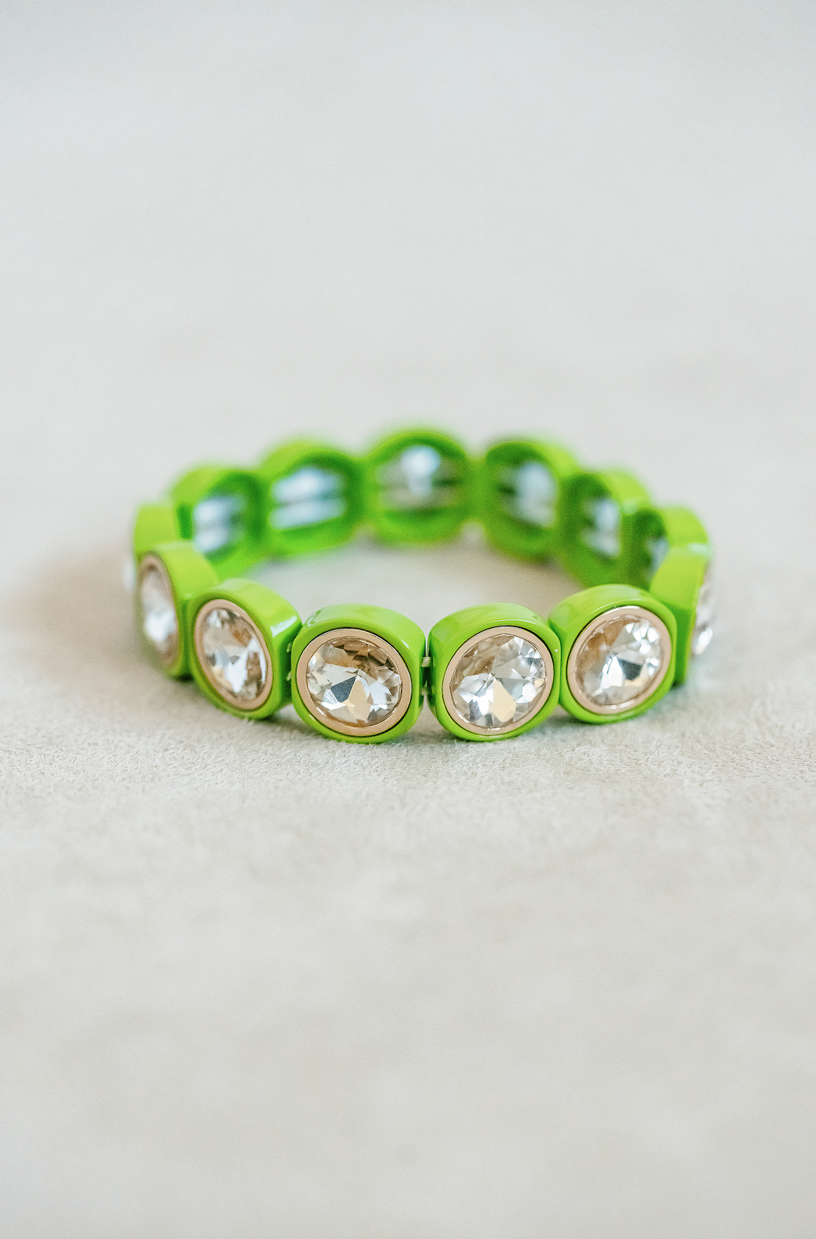 Round acrylic jewel stretch bracelet with gold detailed edging for a complete finish. Adjusts to fit wrist with elastic band in lime green.