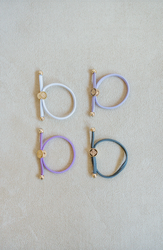 Sold as a set of 4, Children's Size single strand skinny Hair Tie Set are bracelets with round gold end caps and signature gold detail in purple, grey, and white.