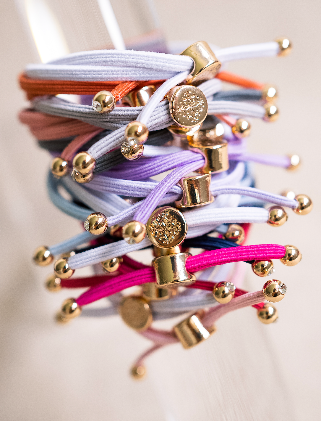 Stack of colorful elastic hair ties with elegant gold accents, showcasing vibrant tones like pink, lavender, and blue, perfect for hair or wrist wear.