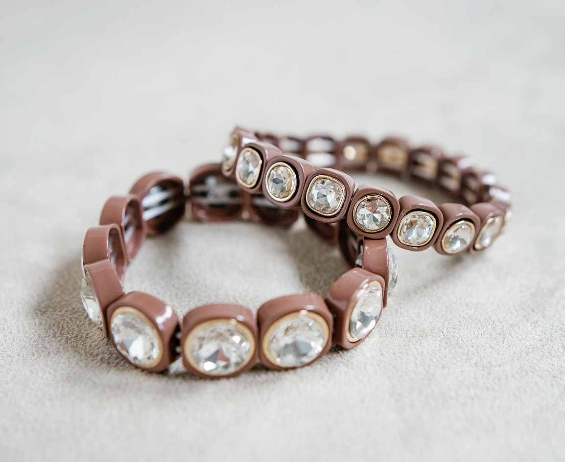 A brown stretch bracelet with glossy square links, each featuring a clear, faceted crystal inset in gold trim, arranged evenly around the band. Round and petite