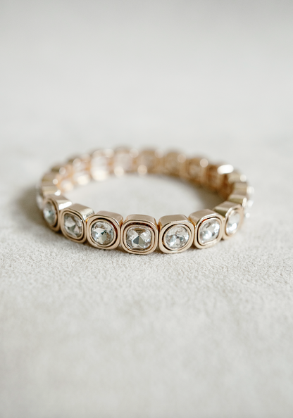 A stretch bracelet with gold-tone square settings, each holding a sparkling round crystal, offering a sleek and luxurious design perfect for layering.