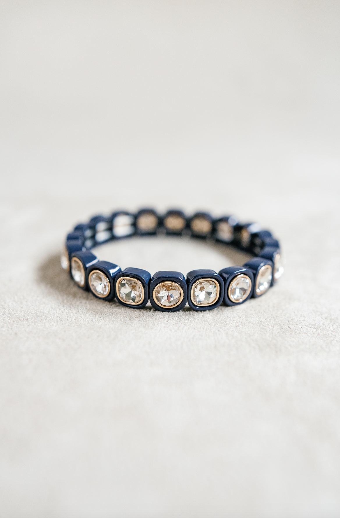 A navy blue stretch bracelet with glossy square links, each featuring a clear, faceted crystal inset in gold trim, arranged evenly around the band.