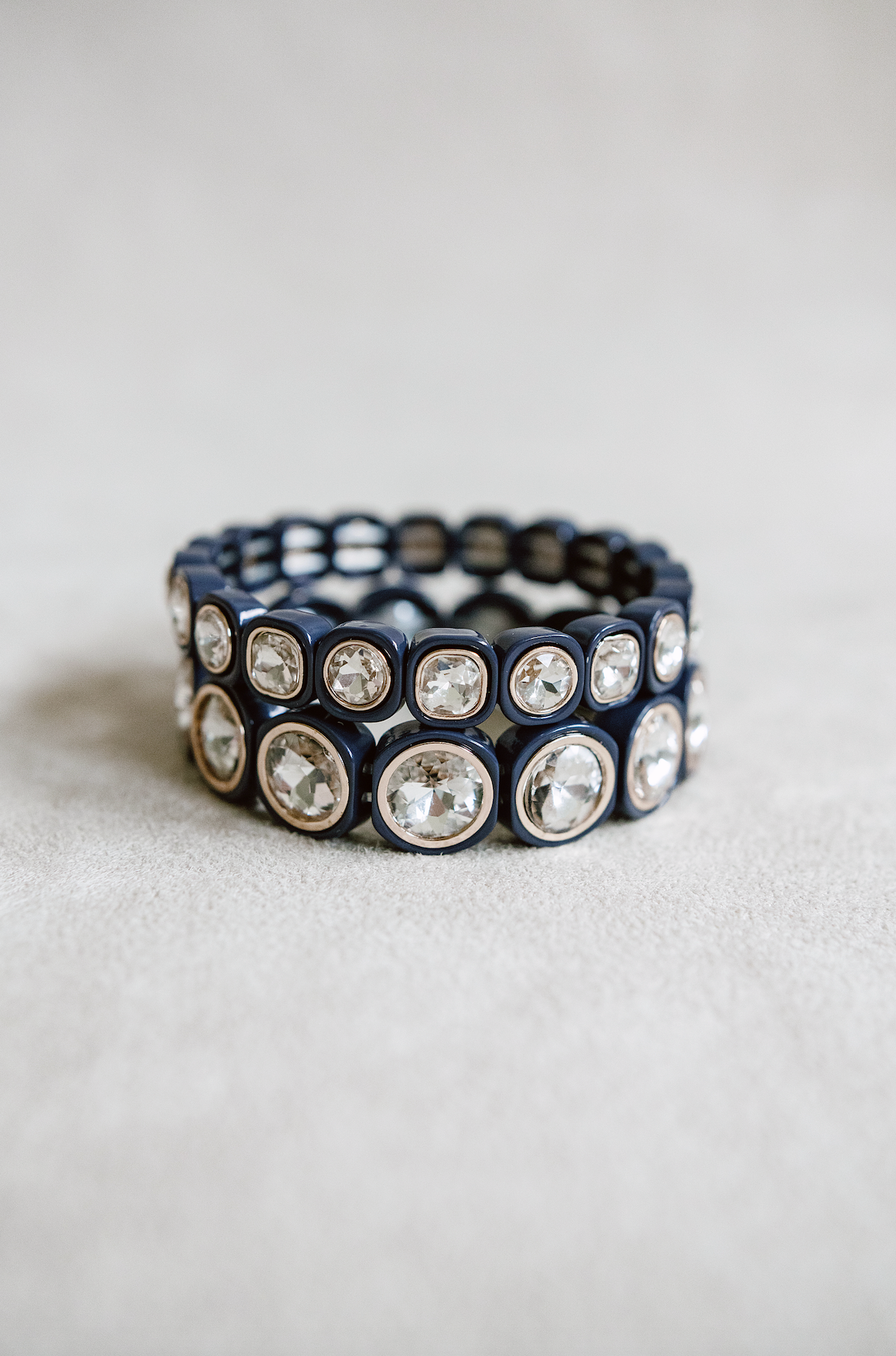 A navy blue stretch bracelet with glossy square links, each featuring a clear, faceted crystal inset in gold trim, arranged evenly around the band. petite and round bracelet stacked