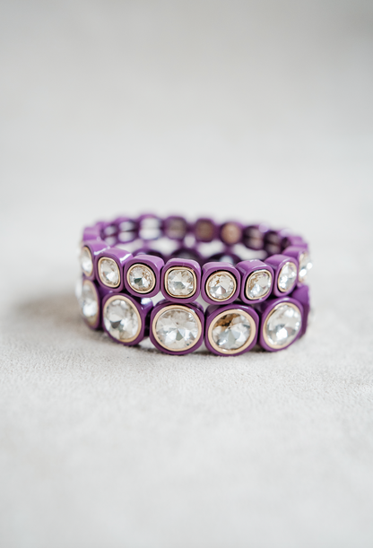 A plum purple stretch bracelet with glossy square links, each featuring a clear, faceted crystal inset in gold trim, arranged evenly around the band. Round and Petite bracelet stack.