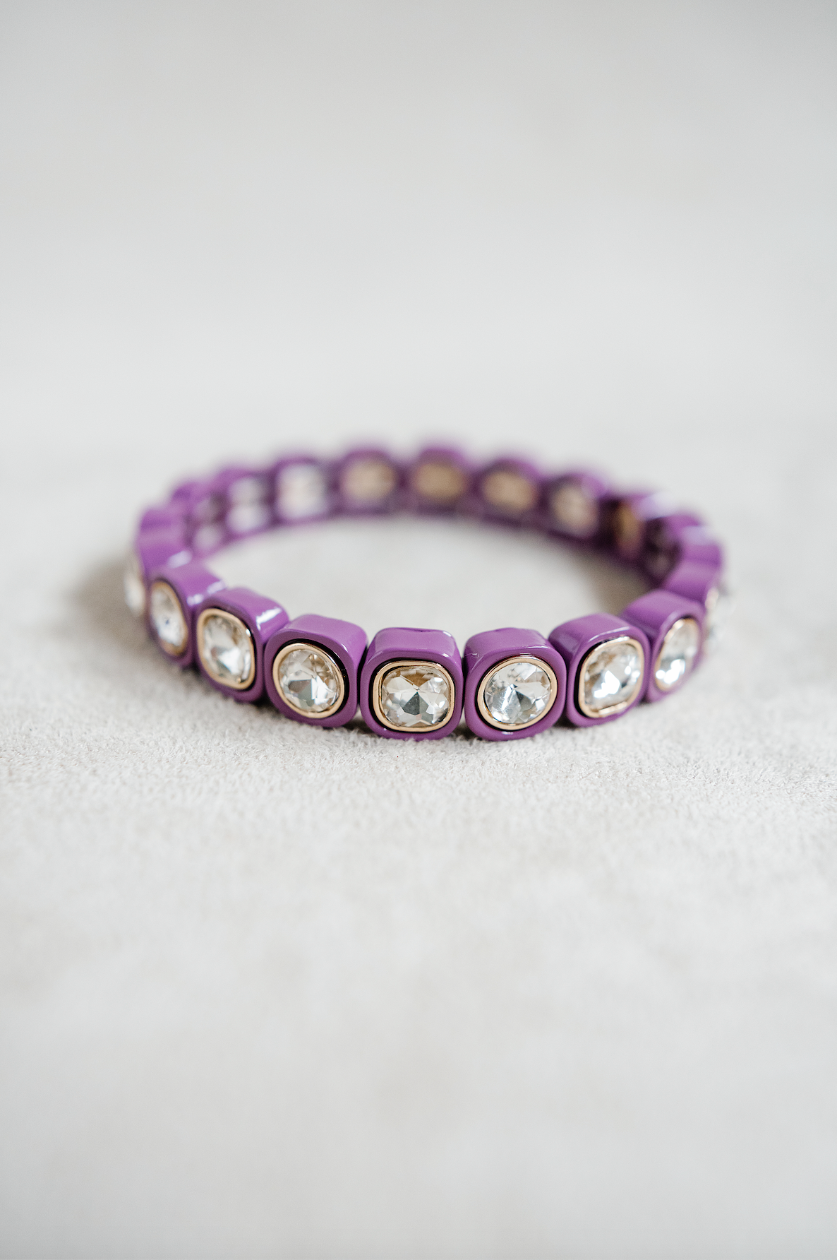 A plum purple stretch bracelet with glossy square links, each featuring a clear, faceted crystal inset in gold trim, arranged evenly around the band.