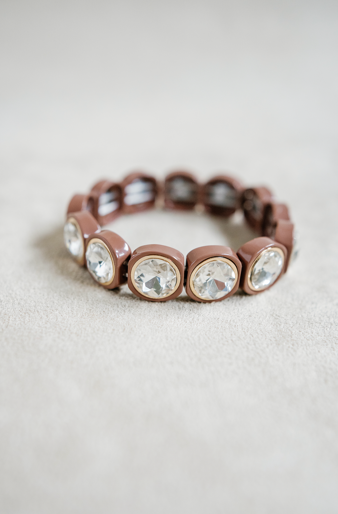 A close-up of a glossy brown bracelet with large, round-cut crystals encased in circular bezels.