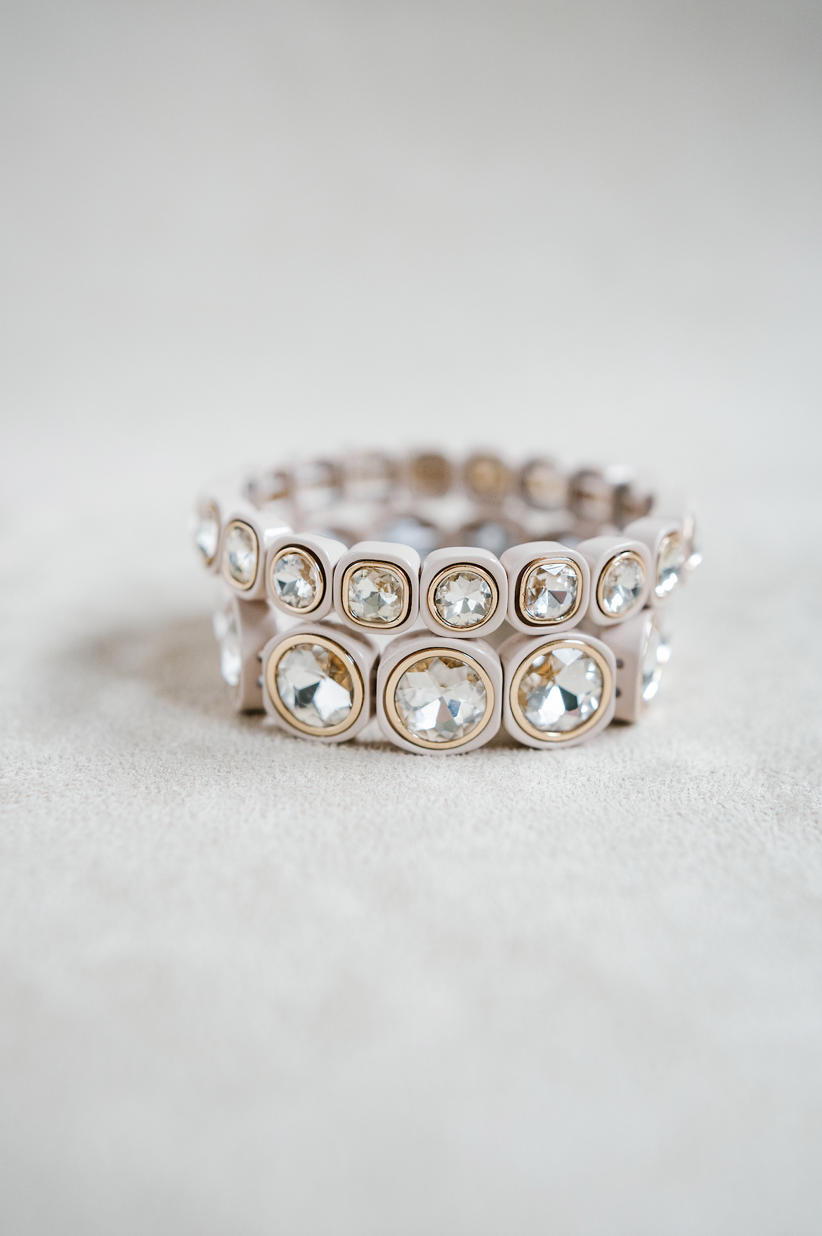 A cream bracelet featuring rounded frames, each holding faceted with rhinestone stones and gold edge for a timeless look. round and petite bracelet stack.