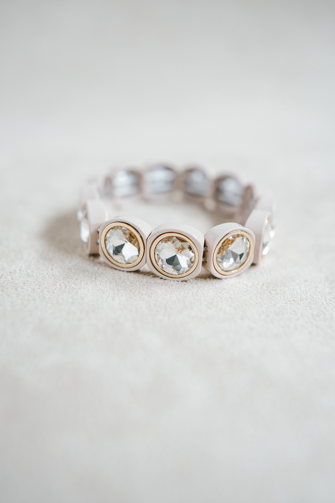 A cream bracelet featuring rounded frames, each holding faceted with rhinestone stones and gold edge for a timeless look.