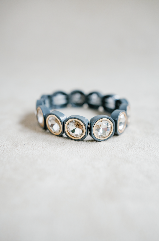 A light gray bracelet featuring large, faceted gemstones framed in gold settings, arranged in a circular, stretchy design ideal for a snug fit.