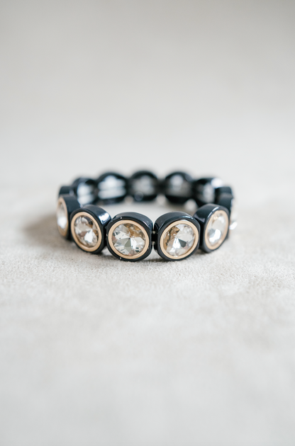 A black bracelet features large, circular crystal stones encased in rounded frames, evenly spaced with elastic threading for flexibility and shine.