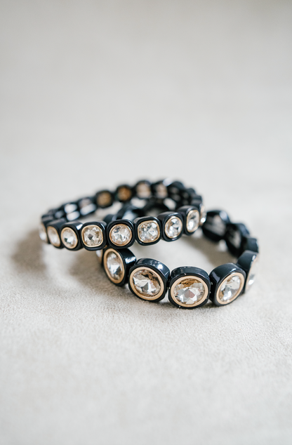 A black bracelet features large, circular crystal stones encased in rounded frames, evenly spaced with elastic threading for flexibility and shine. Petite and Round stretch bracelet.