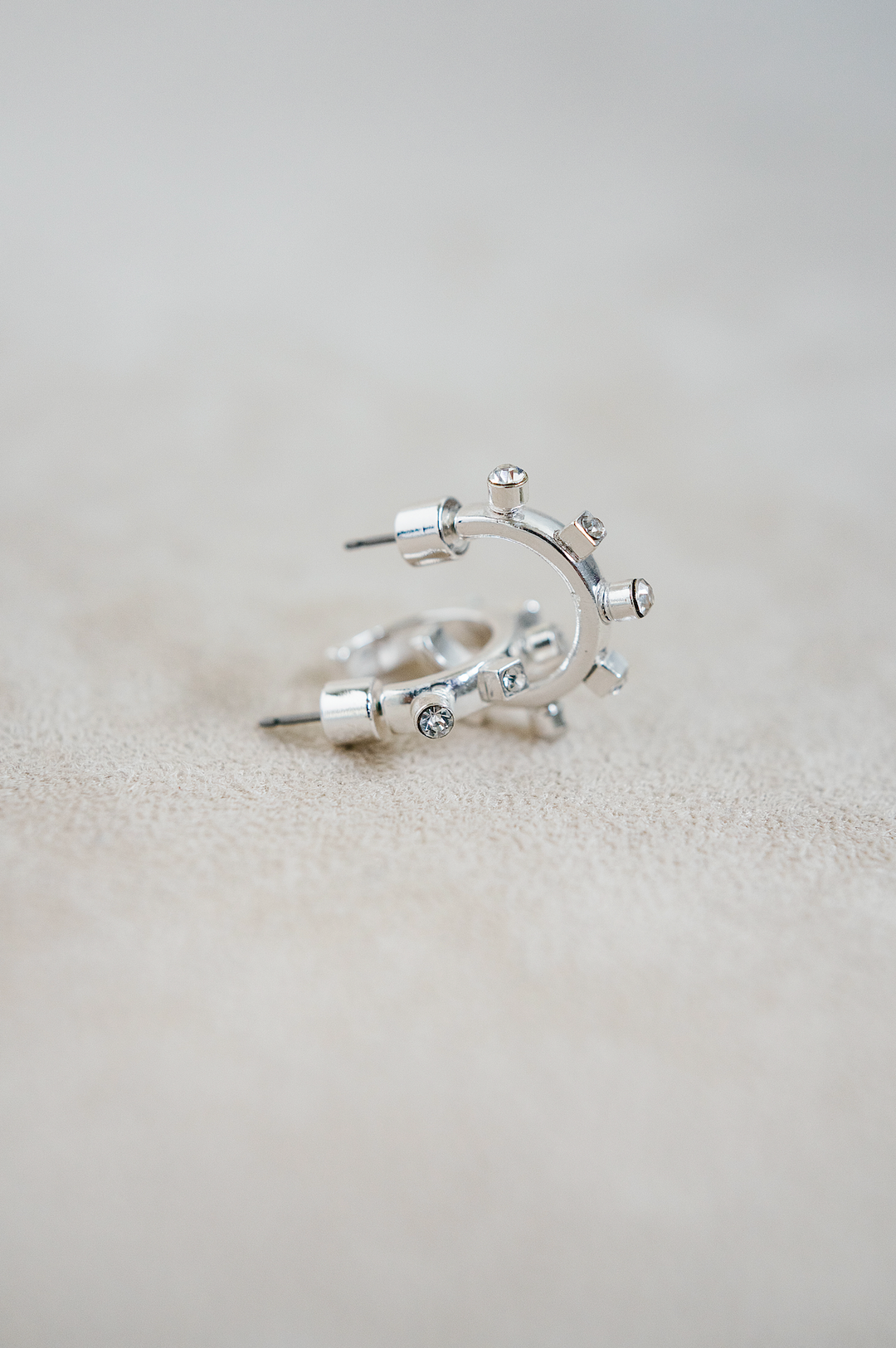 A close-up view of two silver hoop earrings with unique bolt-shaped jewel details arranged around the outer edge.